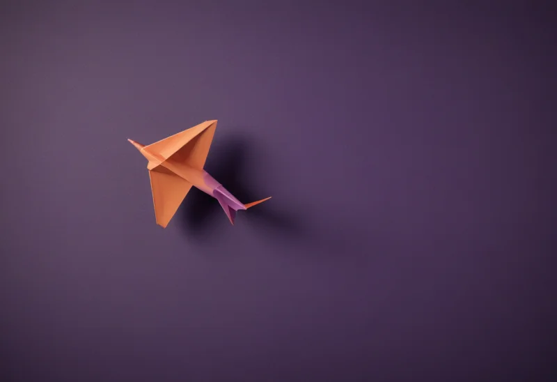 A paper airplane caught in mid-glide, nose tilted slightly upward